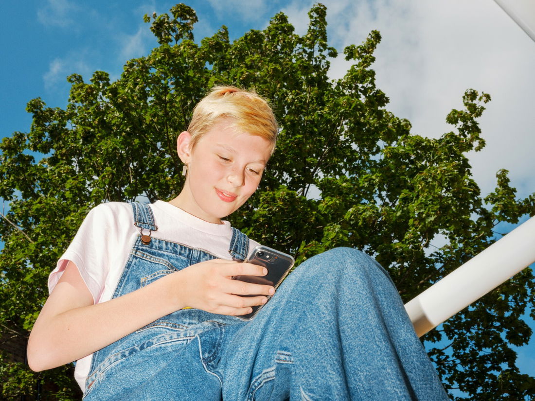 Barneombudet: ungdom sitter på et lekestativ med mobilen i hånden