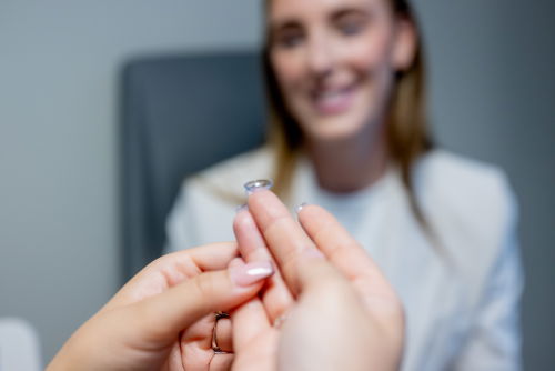 Bilde av hånd med linse og et ansikt som smiler i bakgrunnen