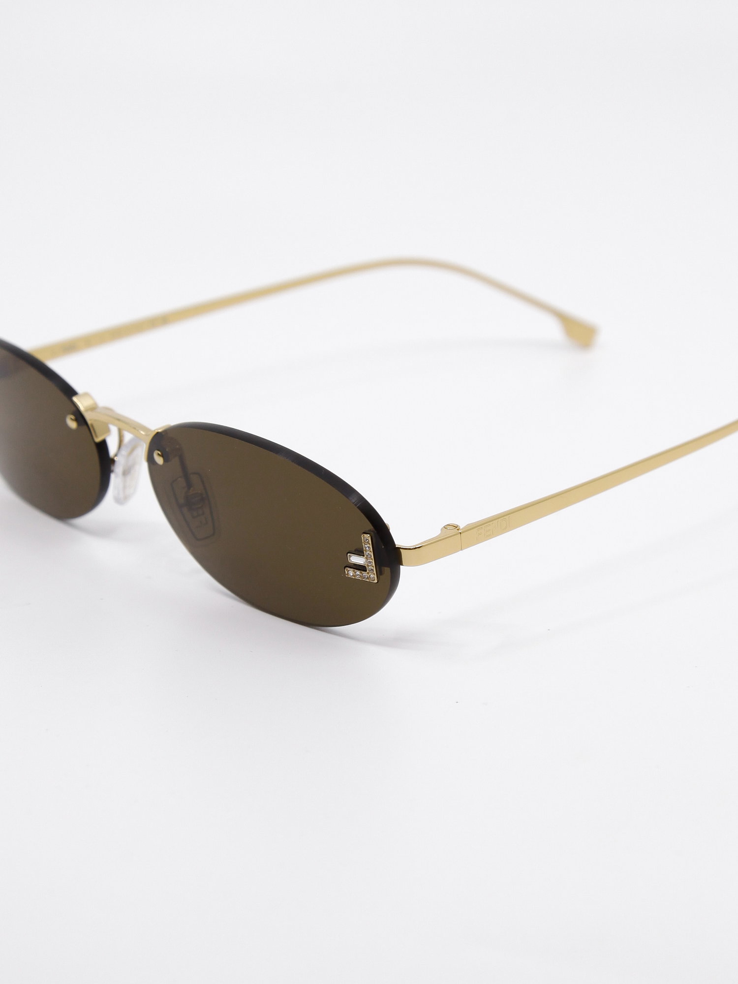 Oval metallsolbrille i gull med  glitrende logo-detalj på glasset