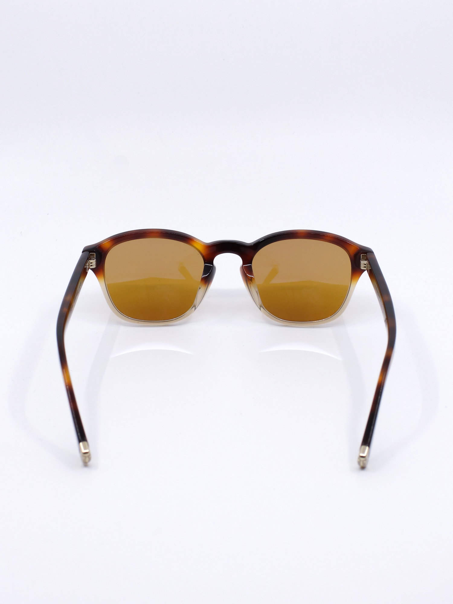 Stilig solbrille fra Brunello Cucinelli med firkantet fasong, med lette avrundede kanter. Solbrillen har en ramme med brun farge i øvre del som går over i en lys, transparent nedre del. Brune solbrilleglass og metalldetaljer i gull.