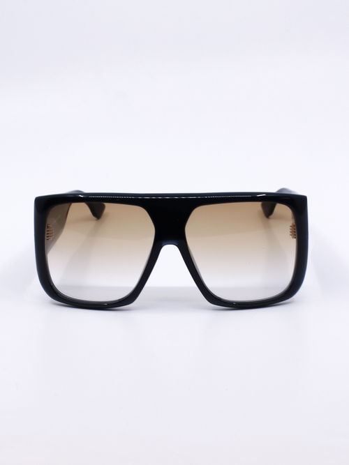 Solbrille med oversized fasong, kraftig svart ramme og brune, graderte glass
